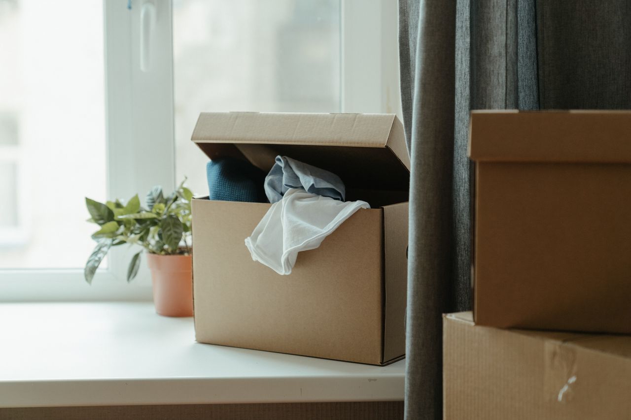 gallery-2 Open cardboard box with clothes by window, symbolizing moving or relocation.