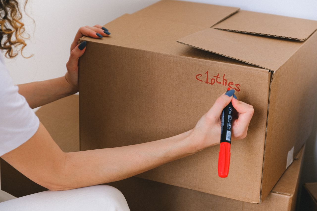 about-01 Close-up of a woman labeling a cardboard box with a red marker indoors.